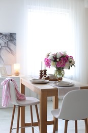Photo of Beautiful table setting with bouquet of peonies in dining room. Interior design