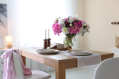 Photo of Beautiful table setting with bouquet of peonies in dining room. Interior design