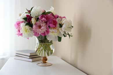 Photo of Bouquet of beautiful peonies and books on white table indoors. Interior design