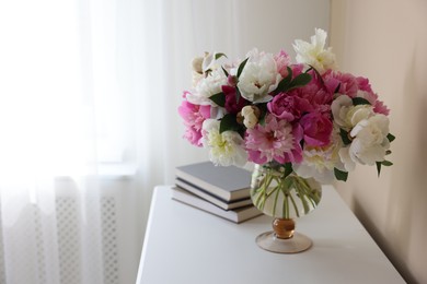 Photo of Bouquet of beautiful peonies and books on white table indoors, space for text. Interior design