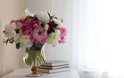 Photo of Bouquet of beautiful peonies and books on white table indoors, space for text. Interior design