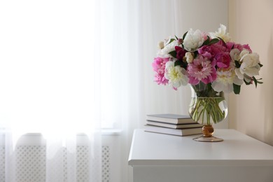 Photo of Bouquet of beautiful peonies and books on white table indoors, space for text. Interior design