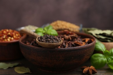 Photo of Different aromatic spices on wooden table against brown background, closeup