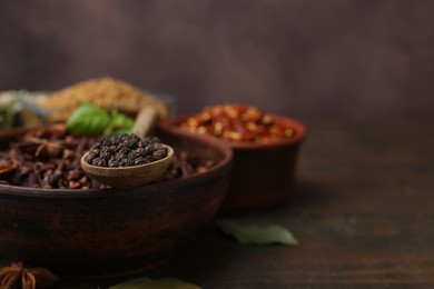Photo of Different aromatic spices on wooden table against brown background, closeup. Space for text