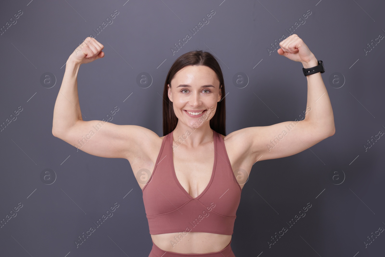 Woman in fitness clothes showing her biceps on grey background Photo of Woman in fitness clothes showing her biceps on grey background