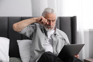 Photo of Senior man with vision problem using laptop on bed at home