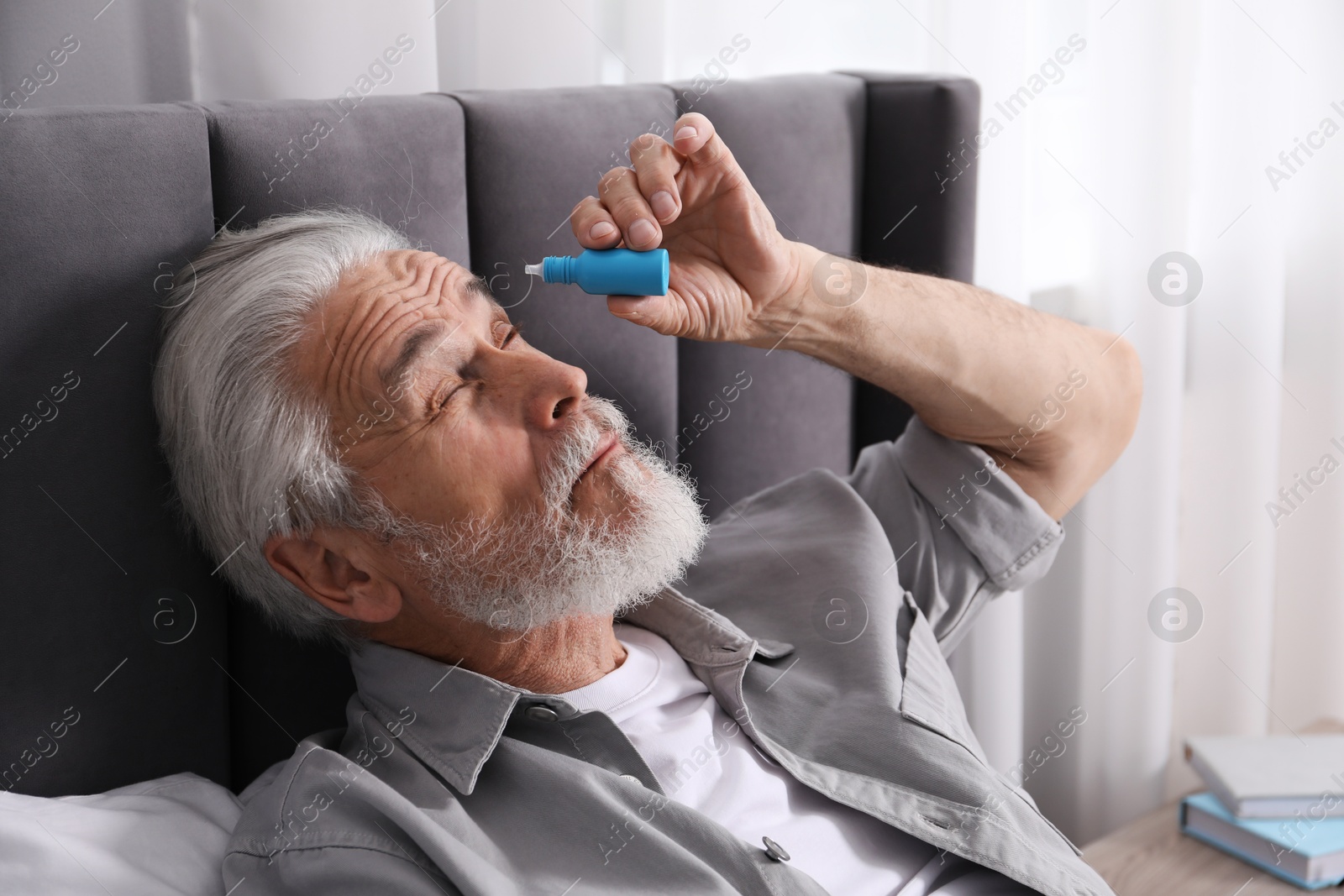 Senior man applying eye drops on bed at home Photo of Senior man applying eye drops on bed at home