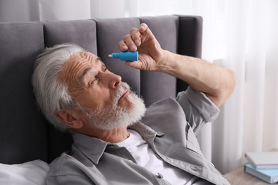 Photo of Senior man applying eye drops on bed at home