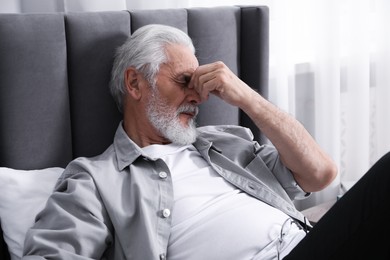 Photo of Senior man suffering from eyestrain on bed at home