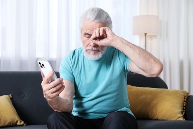 Photo of Senior man with vision problem using smartphone on sofa at home