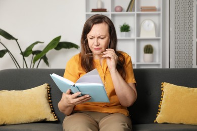 Photo of Woman with vision problem reading book on sofa at home