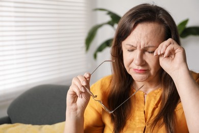 Photo of Woman with glasses suffering from eyestrain on sofa at home, space for text