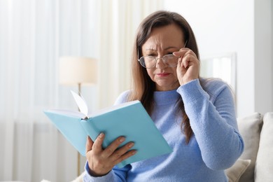 Photo of Woman with vision problem reading book on sofa at home