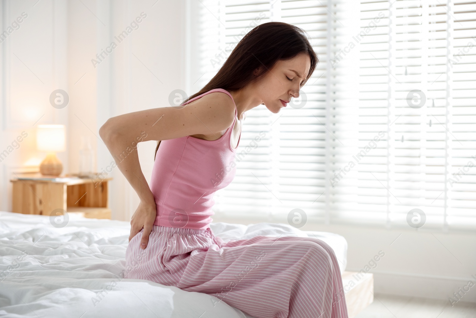 Woman suffering from back pain on bed with soft mattress at home Photo of Woman suffering from back pain on bed with soft mattress at home