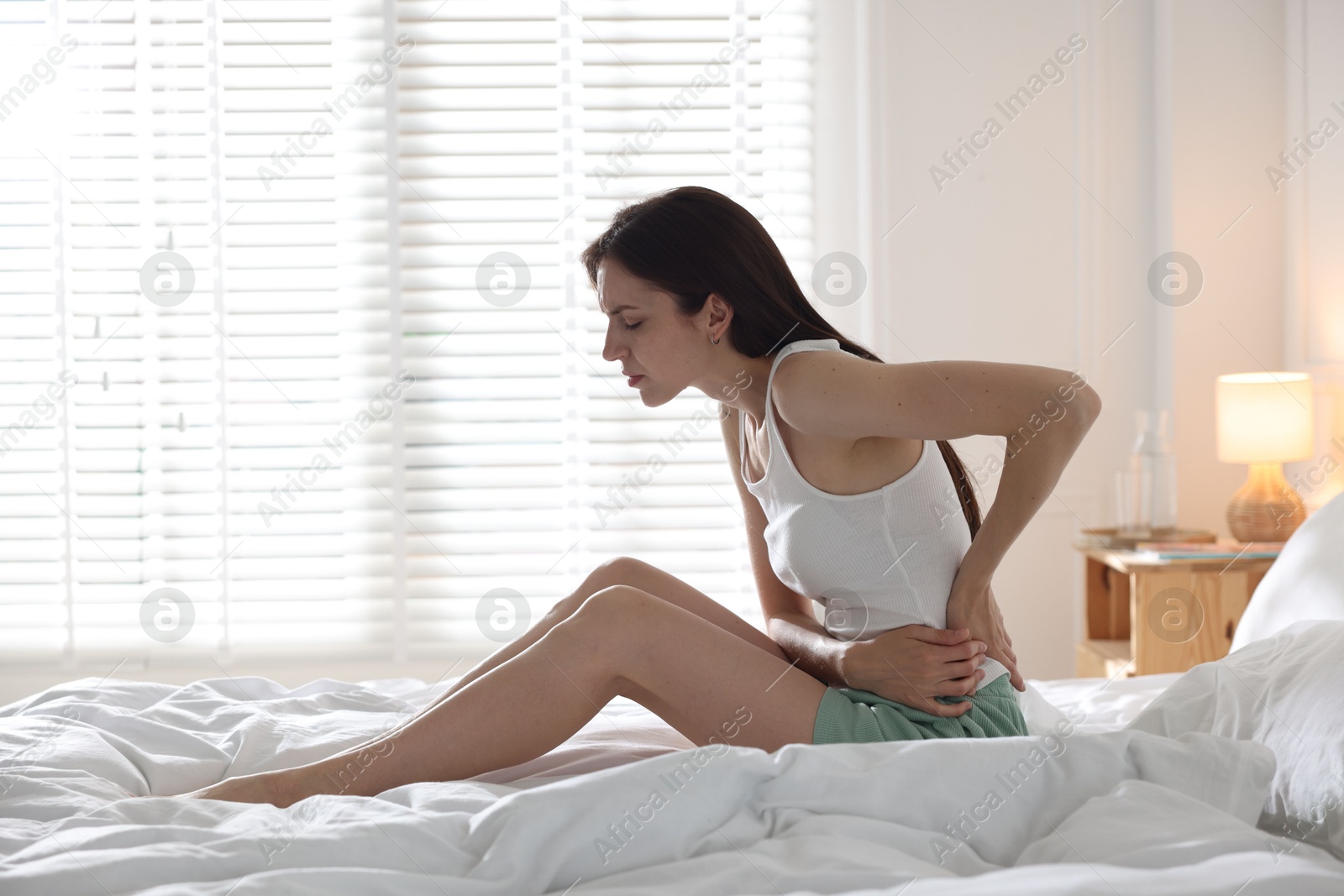 Woman suffering from back pain on bed with soft mattress at home. Space for text Photo of Woman suffering from back pain on bed with soft mattress at home. Space for text