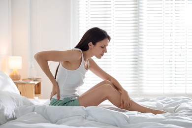 Photo of Woman suffering from back pain on bed with soft mattress at home. Space for text