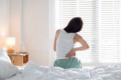 Photo of Woman stretching on bed with soft mattress at home, back view