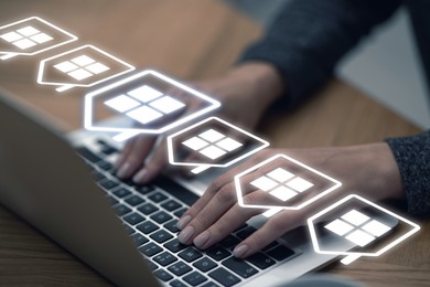 Image of Real estate agent looking for house via laptop at wooden table, closeup. Illustrations of buildings over device