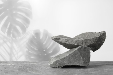 Image of Podium for product presentation made of stones against white background with shadow of leaves. Space for design