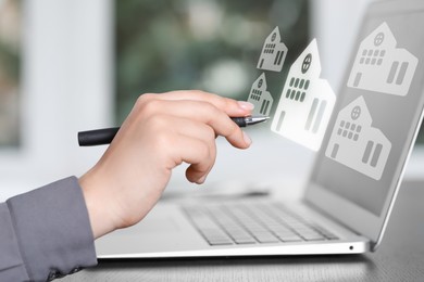 Image of Real estate agent touching house icon on virtual screen above laptop at table, closeup. Search for housing