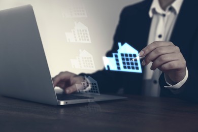 Image of Real estate agent touching house icon on virtual screen while working on laptop at table, closeup. Search for housing