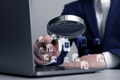 Image of Real estate agent looking at buildings icons with magnifying glass over laptop, closeup. Search for housing