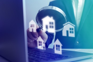 Image of Real estate agent looking at buildings icons with magnifying glass over laptop, closeup. Search for housing