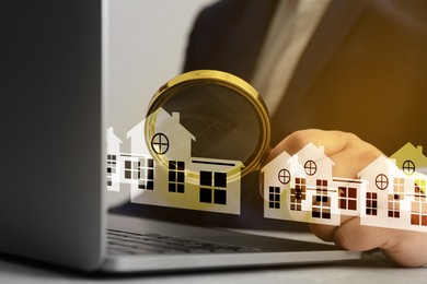 Image of Real estate agent looking at buildings icons with magnifying glass over laptop, closeup. Search for housing