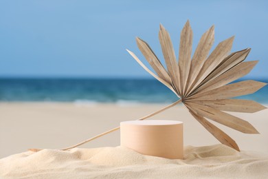 Image of Podium for product presentation with dry palm leaf on sand near blue sea. Stylish promotion poster