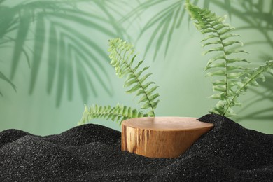 Image of Podium for product presentation with green leaves on black sand against green background. Stylish promotion poster