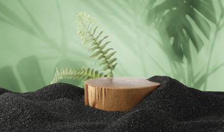 Image of Podium for product presentation with green leaves on black sand against green background, banner design. Stylish promotion poster