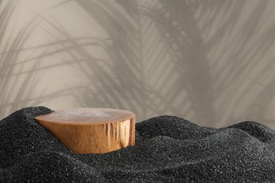 Image of Podium for product presentation on black sand against beige background with shadow. Stylish promotion poster