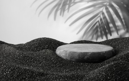 Image of Podium for product presentation. Stone on black sand against white background with shadow of leaves. Stylish promotion poster