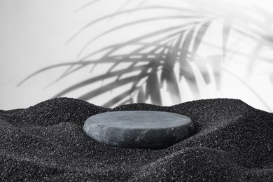 Image of Podium for product presentation. Stone on black sand against white background with shadow of leaves. Stylish promotion poster