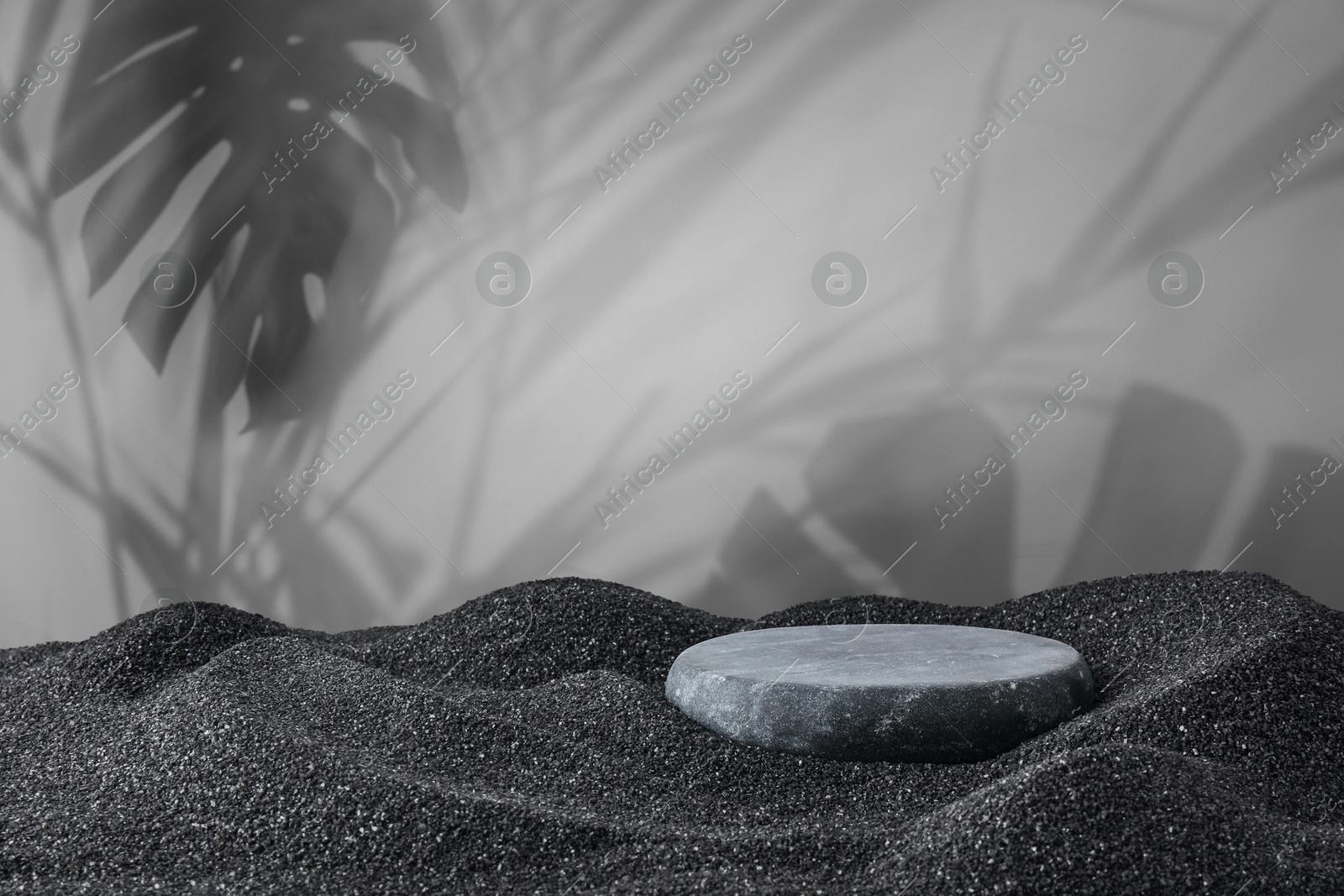 Image of Podium for product presentation. Stone on black sand against grey background with shadow of leaves. Stylish promotion poster