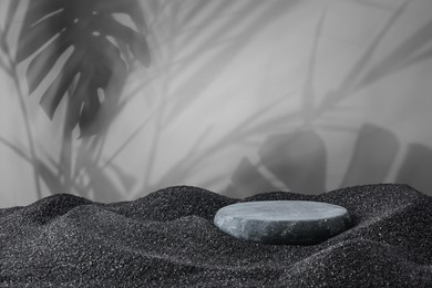 Image of Podium for product presentation. Stone on black sand against grey background with shadow of leaves. Stylish promotion poster