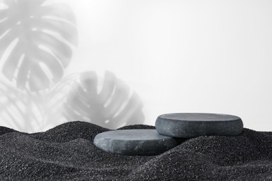 Image of Podium for product presentation. Stones on black sand against white background with shadow of leaves. Stylish promotion poster