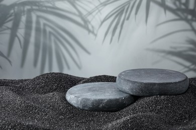 Image of Podium for product presentation. Stones on black sand against grey background with shadow of leaves. Stylish promotion poster