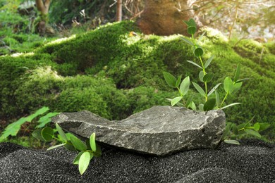 Image of Podium for product presentation. Stone and green branches on black sand in forest. Stylish promotion poster