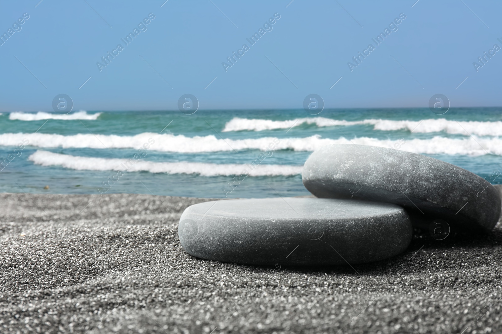 Image of Stones as podium for product presentation on sand. Ocean waves rolling on beach. Stylish promotion poster