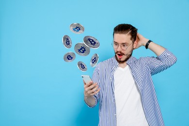 Image of Cryptocurrency. Surprised man using smartphone on light blue background. Bitcoins flying out of device