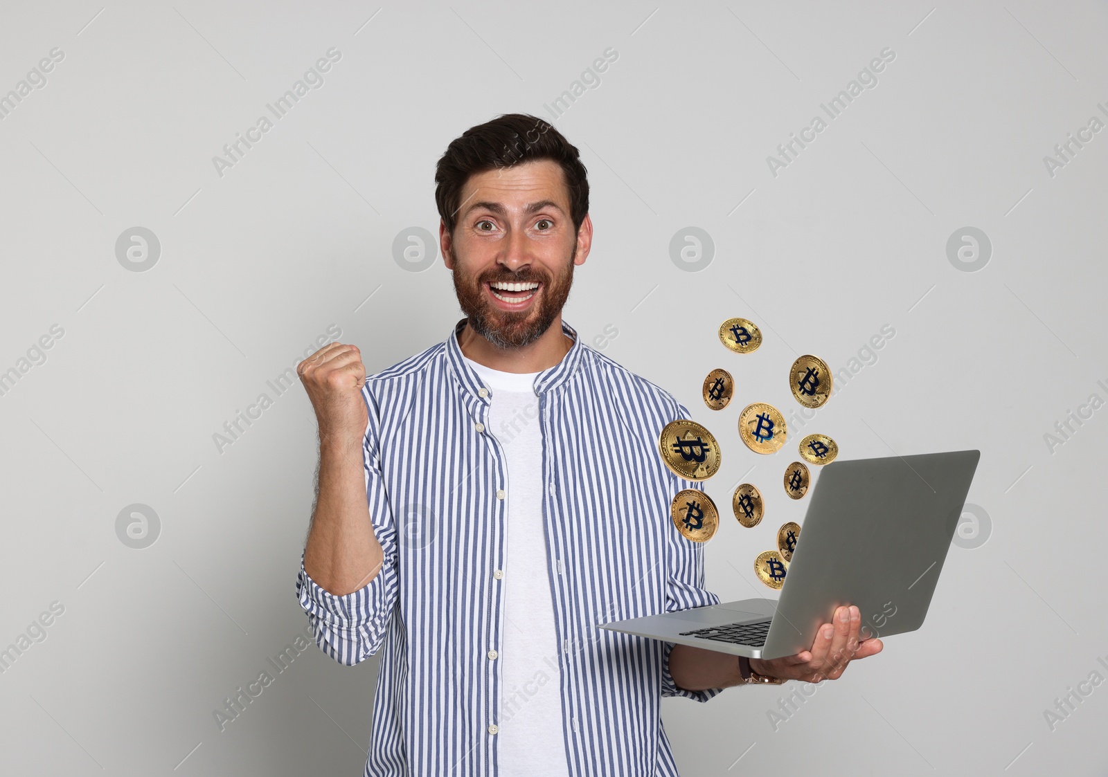 Cryptocurrency. Happy man with laptop on light grey background. Bitcoins flying out of device Image of Cryptocurrency. Happy man with laptop on light grey background. Bitcoins flying out of device