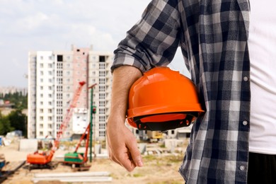 Image of Man with orange hard hat against construction site, closeup. Safety equipment