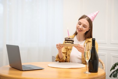 Photo of Birthday celebration. Happy woman with piece of cake having video call via laptop at home