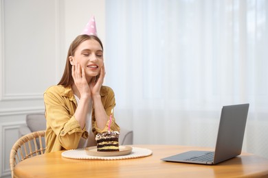 Photo of Birthday celebration. Happy woman with piece of cake having video call via laptop at home
