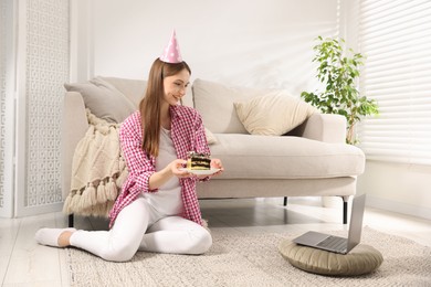 Photo of Birthday celebration. Happy woman with piece of cake having video call via laptop at home