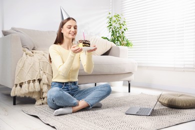 Photo of Birthday celebration. Happy woman with piece of cake having video call via laptop at home