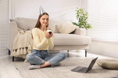 Photo of Birthday celebration. Happy woman with cupcake having video call via laptop at home