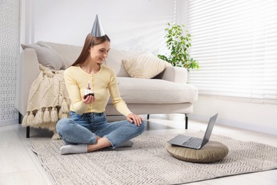 Photo of Birthday celebration. Happy woman with cupcake having video call via laptop at home
