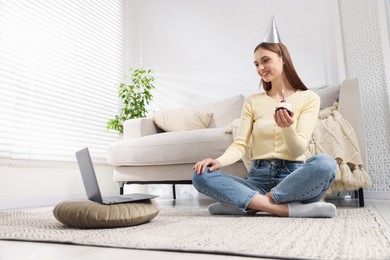 Photo of Birthday celebration. Happy woman with cupcake having video call via laptop at home